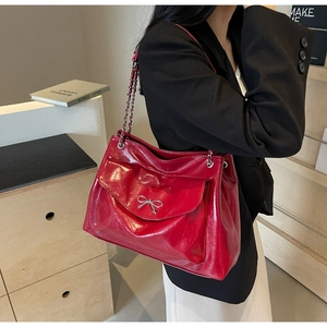 Detail of red glossy leather tote with metal bow and chain strap on a model