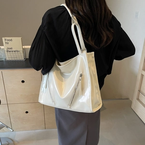 Model wearing a large white patent leather tote bag with functional zipper pockets