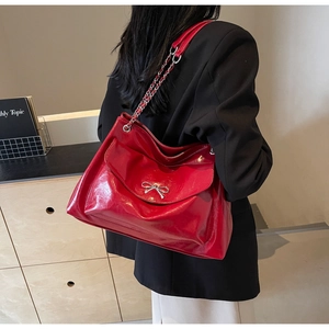 Detail of red glossy tote bag with silver metal bow and braided chain shoulder strap