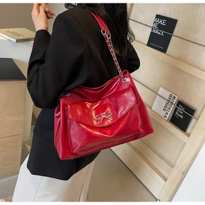 Detail of glossy red leather tote with silver bow metal buckle and chain strap