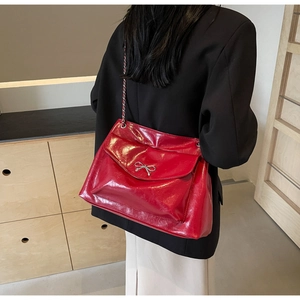 Detail of red patent leather shoulder bag featuring a silver metal bow buckle and chain