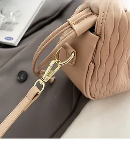 Vue détaillée du crochet doré amovible et de la texture plissée du sac seau couleur beige