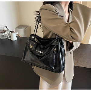 Detailed view of large black patent leather tote with silver bow and chain strap