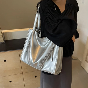 Detail of silver metallic tote bag featuring dual front zippers and wide shoulder straps