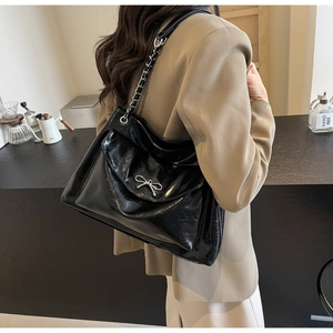 Detail of black glossy patent leather tote with silver metal bow and chain strap