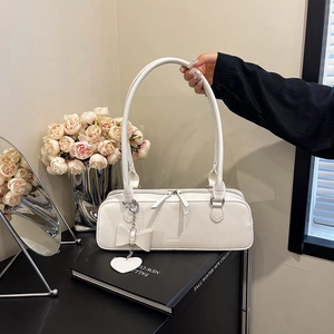 Détail d'un sac à bandoulière rectangulaire crème avec double zip et pendentif noeud