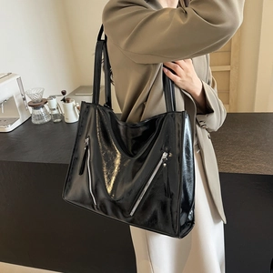 Detailed close-up of glossy black tote bag featuring unique side zipper design and shiny texture
