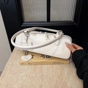 Gros plan d'un sac baguette blanc avec breloques cœur posé sur un livre décoratif
