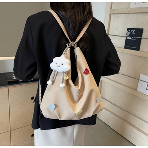 Dettaglio dello zaino in tela beige con toppe a cuore colorate e ciondolo a nuvola