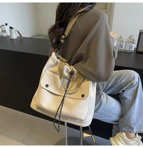 Modèle portant un grand sac fourre-tout en toile crème avec poche avant dans un café