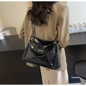 Side view of a glossy black tote bag with silver chain and bow detail on a model
