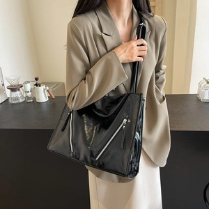 Detail of glossy black tote bag featuring stylish silver diagonal zipper accents