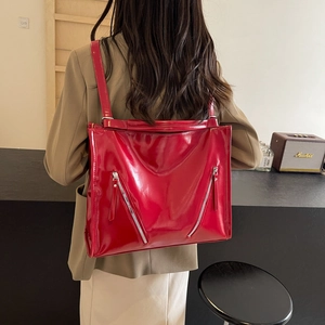 Detail of red patent leather tote bag featuring dual silver zippers and glossy finish