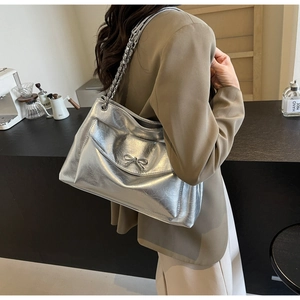 Detail of a silver metallic tote bag with chain strap and bow ornament on a model