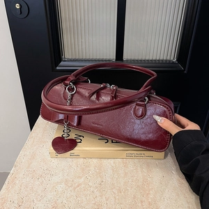 Détail du sac baguette bordeaux avec texture vintage et pendentif cœur sur livre