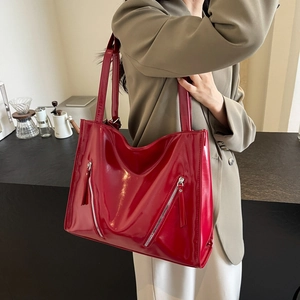 Close-up of a large red patent leather tote bag with decorative zippers on a model