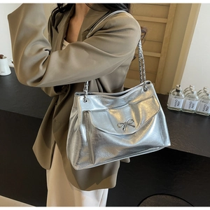 Close-up of shiny silver tote bag with metallic bow detail and chain strap on shoulder