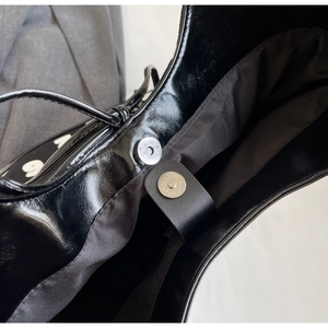 Detailed macro of silver magnetic closures on high-quality black patent leather bucket bag