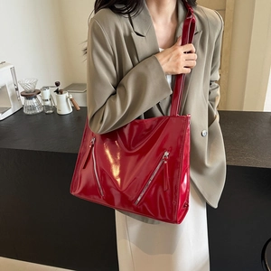 Detail view of large red patent leather tote bag with decorative zippers on grey blazer