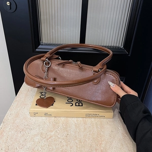 Détail d'un sac à main vintage marron avec nœud et pendentif cœur posé sur des livres