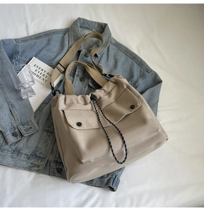 Détail du sac fourre-tout en toile kaki avec poches à rabat sur un fond de veste en jean