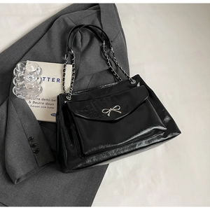 Detail of black glossy tote bag with silver metal bow and retro chain shoulder strap