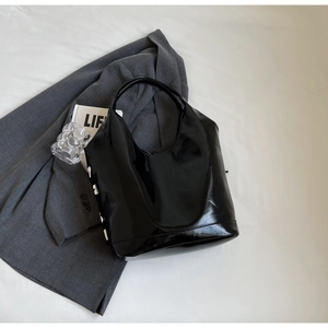 Detailed macro view of high-gloss black patent leather tote bag on grey suit
