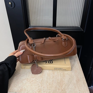 Détail d'un sac à main en cuir marron avec nœud décoratif et pendentif cœur sur livres