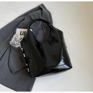 Top view of a large black glossy leather tote bag with white lettering and fashion props