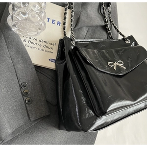 Close-up of black tote bag with silver metal bow and braided chain leather strap