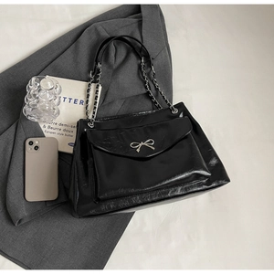 Detail of black glossy tote bag with silver bow accent and leather chain strap