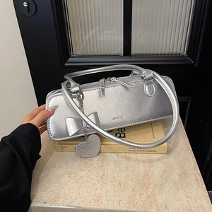 Détail d'un sac à main argenté avec nœud, pendentif cœur et texture métallisée