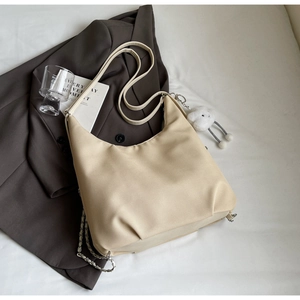 Dettaglio borsa hobo beige con catena argento e ciondolo a nuvola su blazer grigio