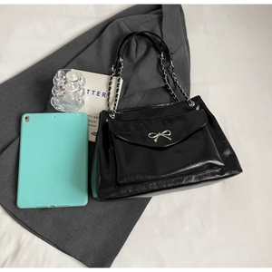 Detailed close-up of glossy black tote bag with silver bow accent and metal chain strap
