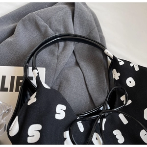 Close-up of canvas shoulder bag featuring white graphic number prints and patent leather handles