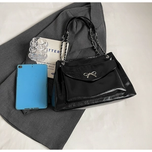 Close-up of black glossy tote bag with silver bow ornament and chain strap detail
