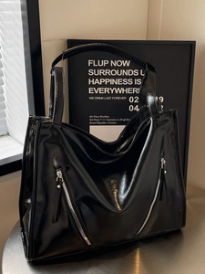Large black glossy tote bag with decorative zippers on metal surface and decor background