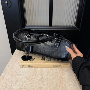 Gros plan du sac en cuir verni plissé noir avec nœud et breloque cœur en métal