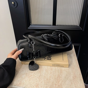 Détail du sac baguette noir brillant avec un nœud décoratif et un pendentif en cœur