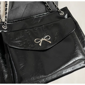 Detail of glossy patent leather tote with silver bow buckle and woven chain strap