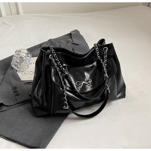 Detailed close-up of glossy black tote bag with silver metal bow and chain strap
