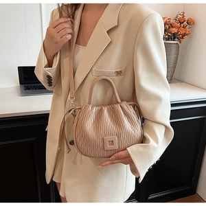 Détail du sac seau plissé beige avec boucle carrée et cordon de serrage porté par un modèle