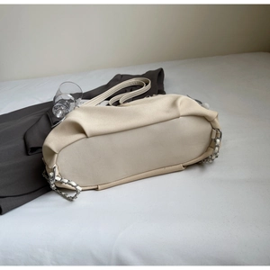 Dettaglio della grande borsa tote in tela beige con tracolla a catena su letto bianco