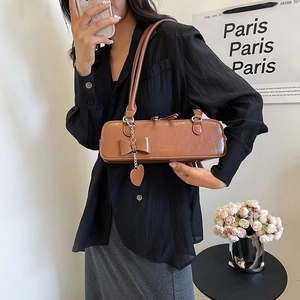 Détail d'un sac à épaule en cuir marron avec un nœud et un pendentif en forme de cœur