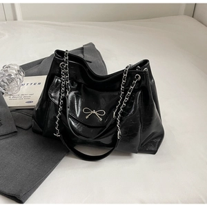 Detail of glossy black leather tote bag featuring a silver bow and metal chain strap