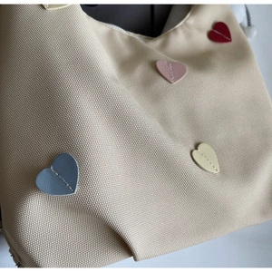 Dettaglio della borsa tote in tela con toppe in pelle a cuore e cuciture di precisione