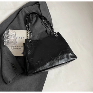 Detail of black pleated tote bag with silver chain strap on a grey suit jacket