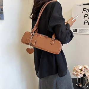 Détail d'un sac porté épaule marron avec un nœud mignon et un pendentif cœur et chaîne argent