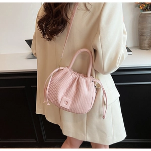 Sac seau plissé rose avec cordon porté par un mannequin en blazer beige élégant
