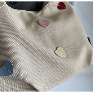 Dettaglio borsa hobo beige con toppe colorate a cuore e finitura in tela testurizzata